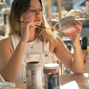 Ana Sayfa 4 Atölye Dally seramik atölyesinde, genç bir kadın el yapımı seramik kupayı özenle fırça ile boyuyor, sanatsal üretim sürecini sergiliyor.